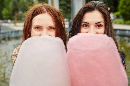 Two cheerful sisters eating cotton candy at the parkの写真素材