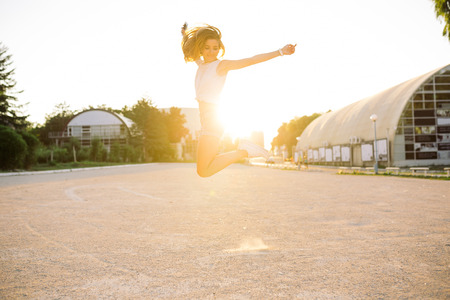 Outdoor summer lifestyle image of young pretty hipster woman having fun, listening music and dancing