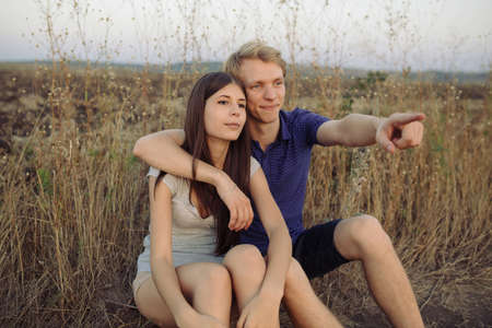 Young couple in love sitting on the grass in the field