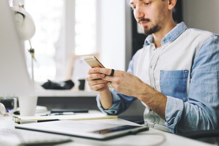 Young man working on computer and using mobile phone while sitting at his working place in office