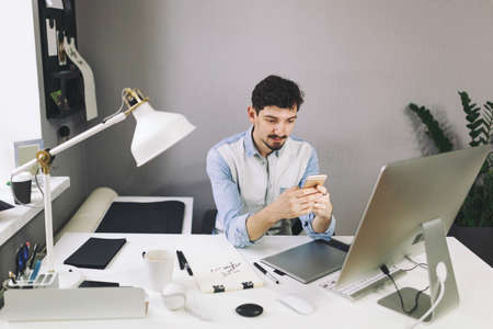 Young man working on computer and using mobile phone while sitting at his working place in office