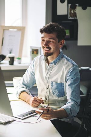 Young man working on computer while sitting at his working place in officeの写真素材