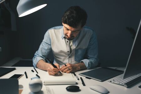 Designer at work in office. Man drawing in note pad