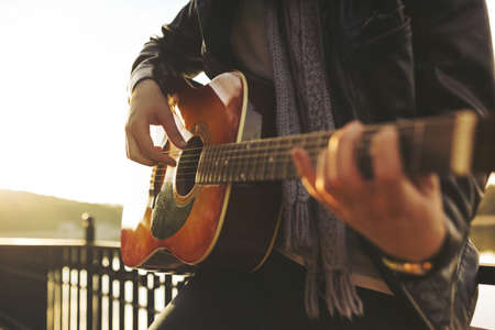 Portrait of young man playing on guitar at the lakeの写真素材