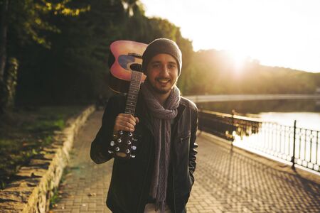 Portrait of young man walks by the lake and holding guitar