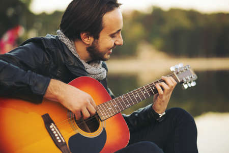 Portrait of young man playing on guitar at the lake