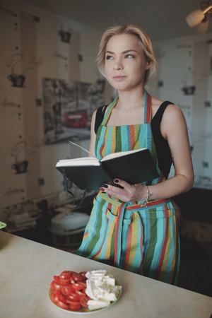 Young woman looking up in a recipes book on the kitchenの写真素材
