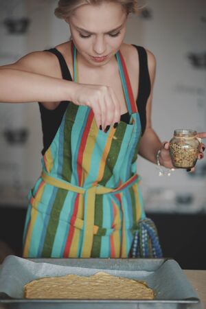 Young blonde woman in color apron cooking pizza at kitchenの写真素材