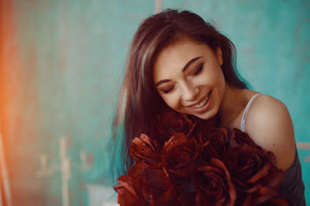 Picture of young and beautiful woman with bouquet of roses in her bedroomの写真素材