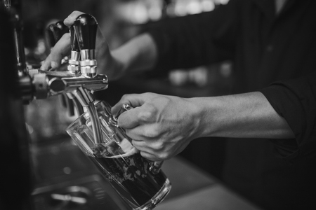 Barman at work in the pub pours beer into a glass. Black and white photo. Close up on handsの写真素材