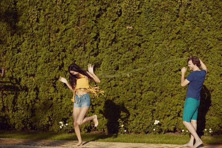 Healthy lifestyle: couple having fun pour each other with garden hose at the swimming poolの写真素材