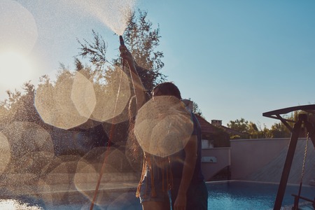 Healthy lifestyle: couple having fun pour each other with garden hose at the swimming poolの写真素材
