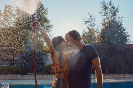 Healthy lifestyle: couple having fun pour each other with garden hose at the swimming poolの写真素材