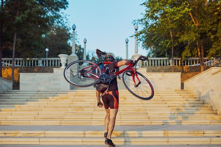 Young and energetic cyclist in the park. Man climbs the stairs holding a bike on his shoulderの写真素材