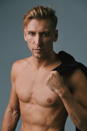 Portrait of a handsome muscular young man posing at studio as fashion model on a gray background with contrast shadowsの写真素材