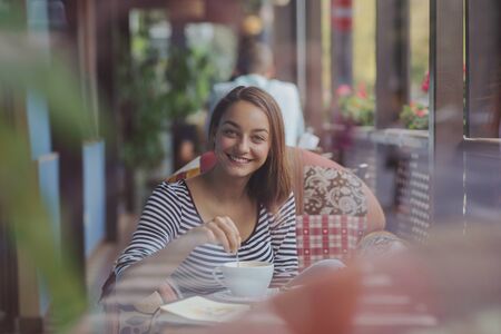 Young woman sitting indoor in urban cafe. Cafe city lifestyle. Casual portrait of teenager girlの写真素材