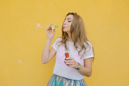 Attractive cute teenage girl against the background of yellow wall make soap bubblesの写真素材