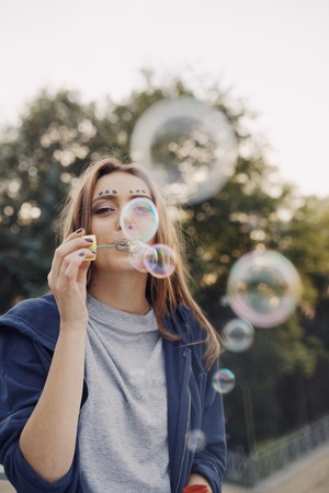 Young pretty girl posing in the street. Sunrise time, happy face woman, cute, attractive, fashion model, hipster style, make soap bubblesの写真素材