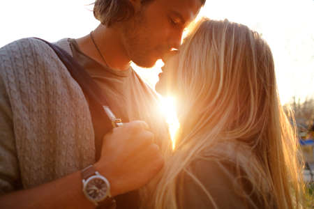 Happy smiling couple in love hug and kiss each other in the amusement park. Sunny warm spring eveningの写真素材
