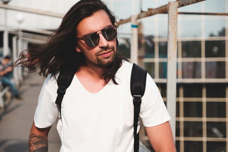 Stylish hipster model with long hair lifestyle in the street. Dressed in a white T-shirt and torn blue jeans in the cityの写真素材