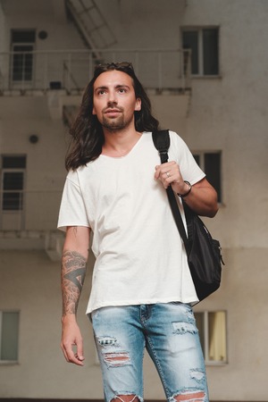 Stylish hipster model with long hair lifestyle in the street. Dressed in a white T-shirt and torn blue jeans in the cityの写真素材