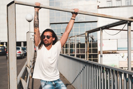 Stylish hipster model with long hair lifestyle in the street. Dressed in a white T-shirt and torn blue jeans in the cityの写真素材