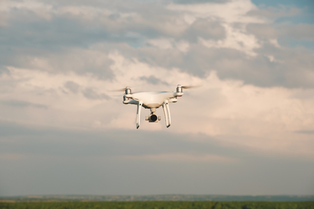 White drone hovering in a bright blue sky. Drone copter flying with digital cameraの写真素材