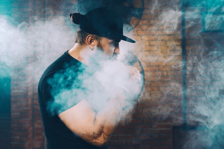 Vaping man wearing a hat, obscured behind a cloud of vaporの写真素材