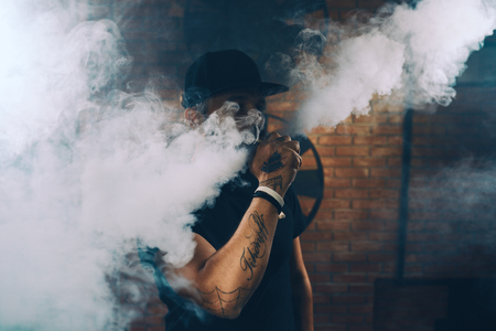 Vaping man wearing a hat, obscured behind a cloud of vaporの写真素材