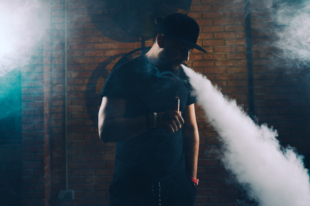 Vaping man wearing a hat, obscured behind a cloud of vaporの写真素材