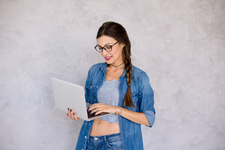Feeling good woman in eyeglasses standing  focused to the laptopの写真素材