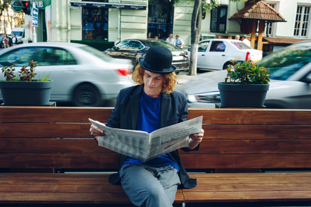 Red haired hipster man sitting on bench with newspaperの写真素材