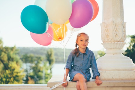 Cute girl portrait holding colorful balloons in the city parkの写真素材