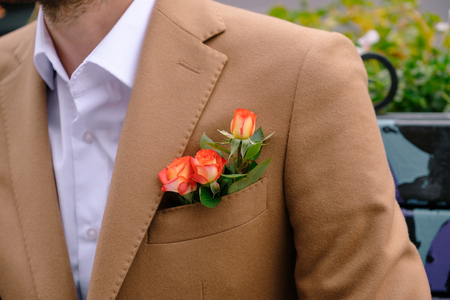 Close-up man dressed in classy vintage camel jacket with three red yellow roses in pocket. Man ready for a special event, wedding, dating, fashion presentation.の写真素材