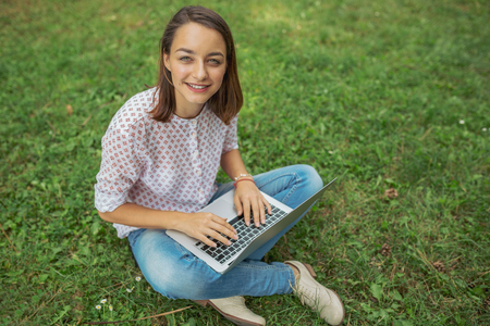 Young woman with laptop sitting on green grassの写真素材