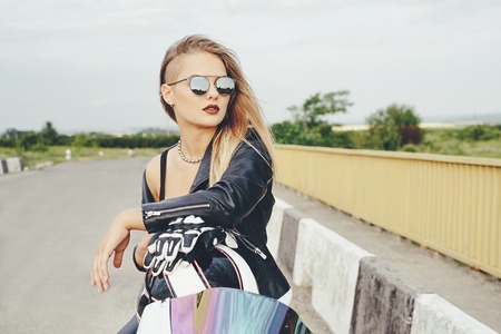 Attractive young woman posing on a motorbike wearing fashionable sunglasses, leather jacket, stylish haircut. Confident face expression, hairstyle, sensual biker female, portraitの写真素材