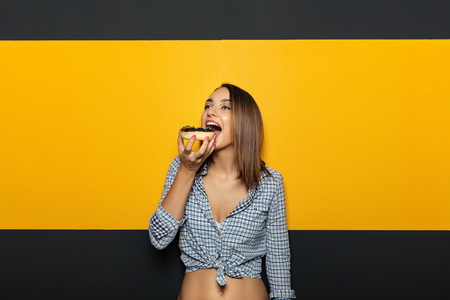 Young beautiful woman with a white, bright smile eating tasty donut. Copy space on colorful background. Small life pleasures.の写真素材