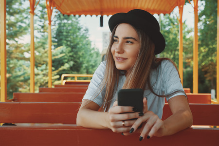 Young hipster girl in trendy hat holding smartphone in hands smi