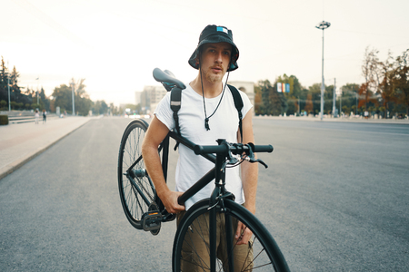 Portrait of a blonde white man in the city with a classic bike on shoulder, looking to camera while standing on a road in the cityの写真素材