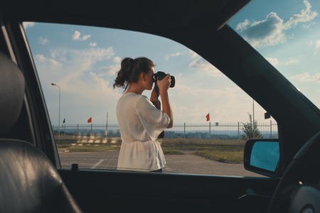 Female driver taking picture during her journey. Carefree lady has stopped in the parking lot to immortalize the amazing sky.の写真素材