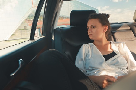 Modern Woman Sitting In Rear Seat Of Car On Road Trip Relaxingの写真素材