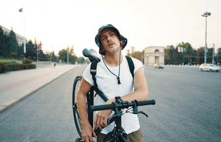 Portrait of a blonde white man in the city with a classic bike on shoulder, looking to camera while...