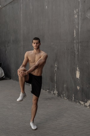 Handsome, athletic man warming up stretching before the training, with gray walls in the background. Healthy lifestyle and sportswear advertising.の写真素材