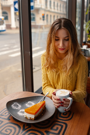 Pretty young woman enjoying a cup of coffee and a slice of delicious cake while resting, the sunlight shines through the window in the cafe.の写真素材