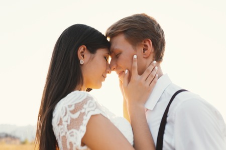 Loving couple dressed in white, ready to kiss outdoors with closed eyes, touching, gentle each other in sunlight on a white background outdoors - Concept about people, love and lifestyleの写真素材