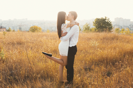 Loving couple dressed in white kissing outdoors, touching, gentle each other with a beautiful landscape in background, golden grass - Concept about people, love and lifestyleの写真素材