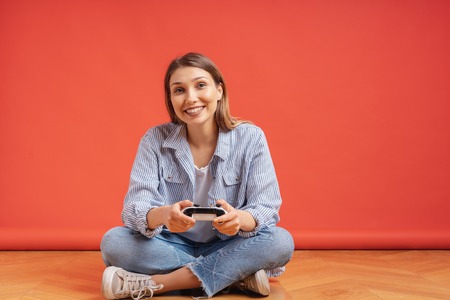 Excited delighted woman playing video games, while holding a game console in hands and sitting...
