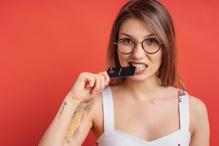 Cropped portrait of pretty girl holding with hand a plastic credit card between her teeth isolated...