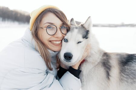 Happy young girl playing with siberian husky dog in winter park. They walk on a frozen lakeの写真素材