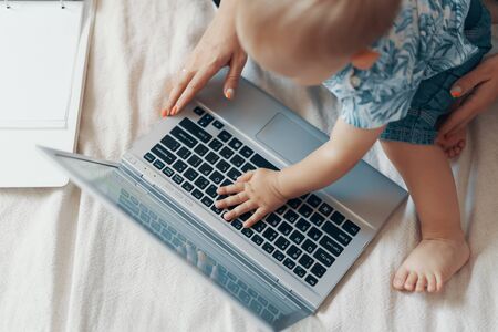 Young mother with her child working on laptop in bedroom at home. Multi-tasking, freelance and...
